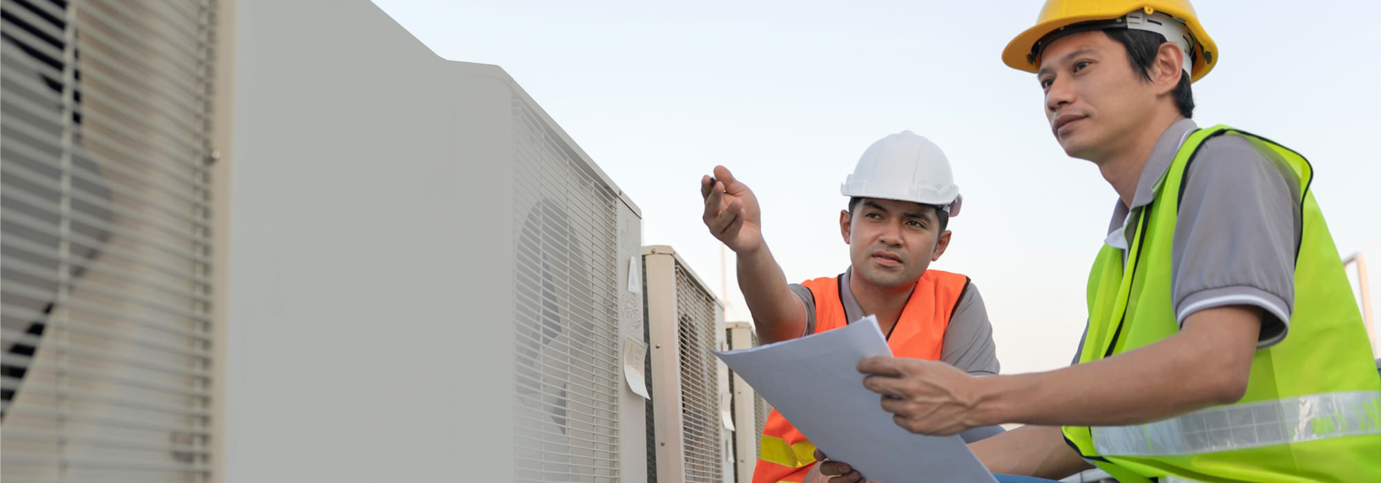 Technicians discussing air conditioning units while on a rooftop