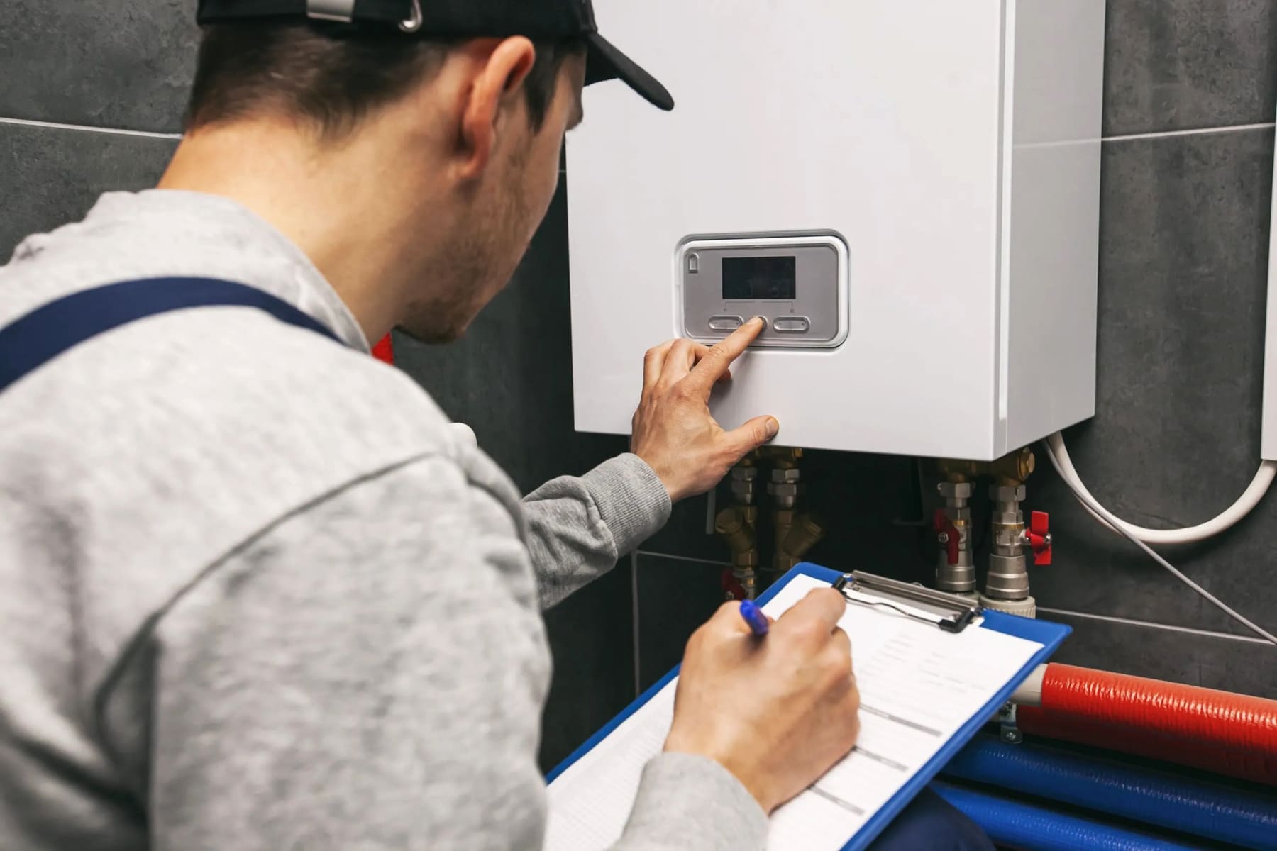 Technician is examining the heating system in the boiler room while holding a clipboard